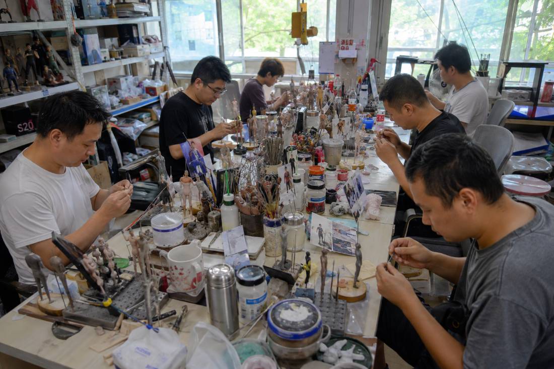 The long studio bench mid-batch, figurines in progress